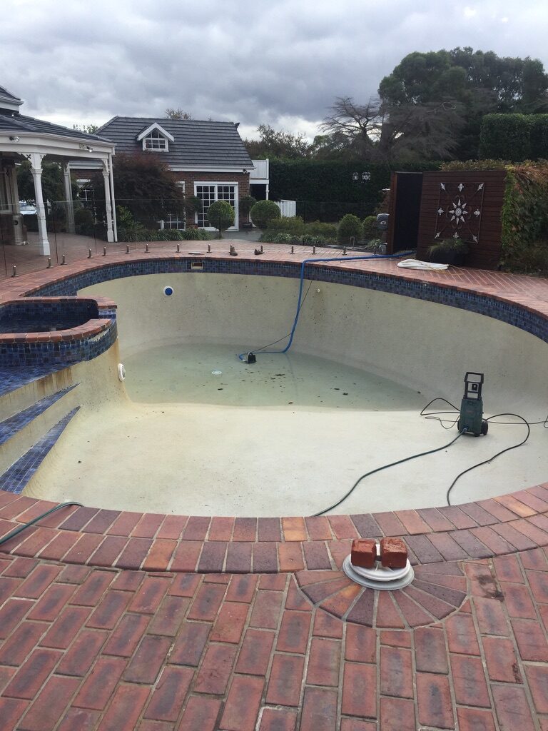 Drained concrete pool with worn, faded surface before epoxy resurfacing
