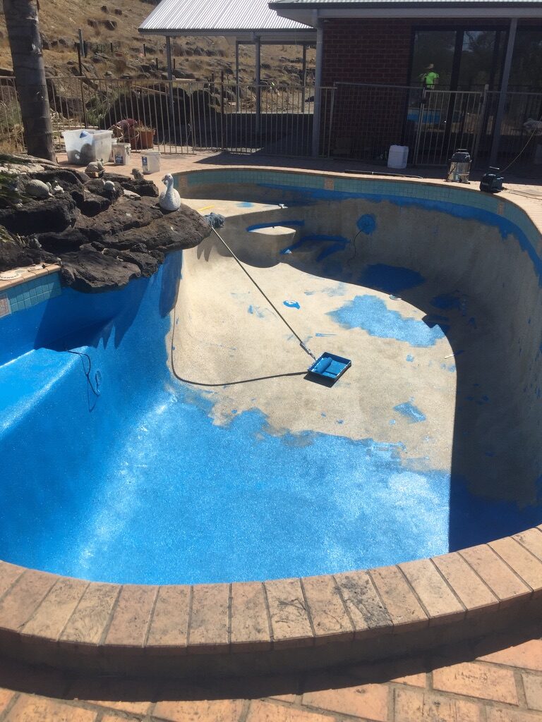 Same pool part-way through epoxy coating, blue finish going down over the pebblecrete