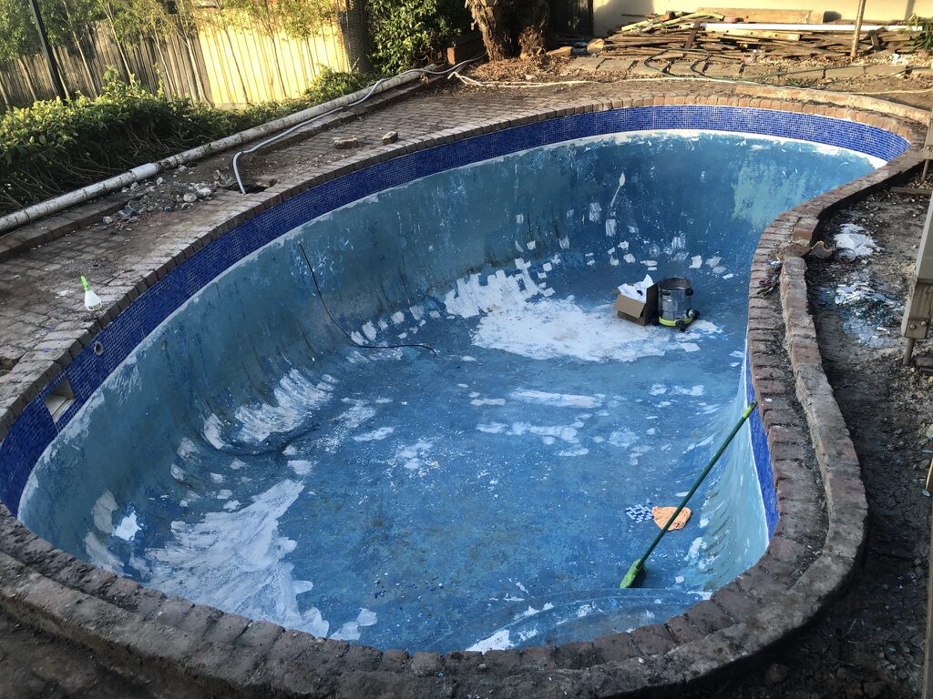 Kidney-shaped pool with old peeling paint before resurfacing